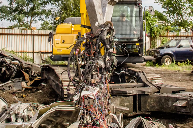 Wiring and tubing being removed from scrap car with KOBELCO SK210D-11 Car Demolition Excavator
