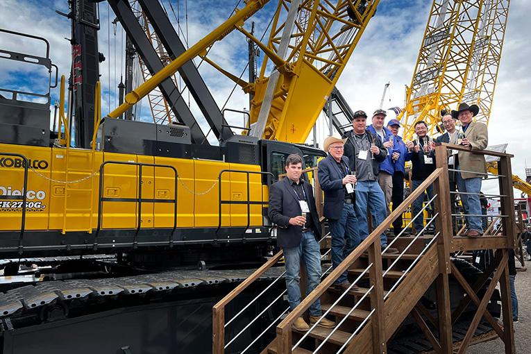 Group of people toasting together on a stage in front of a large crane
