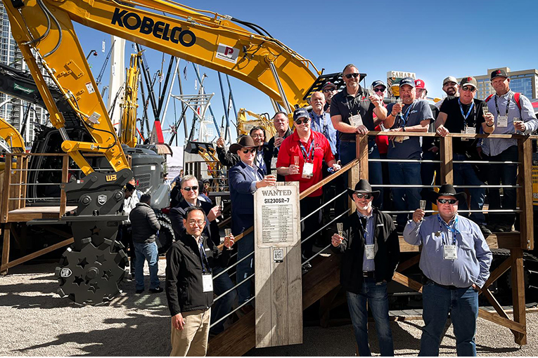 Group of people toasting together on a stage in front of an excavator