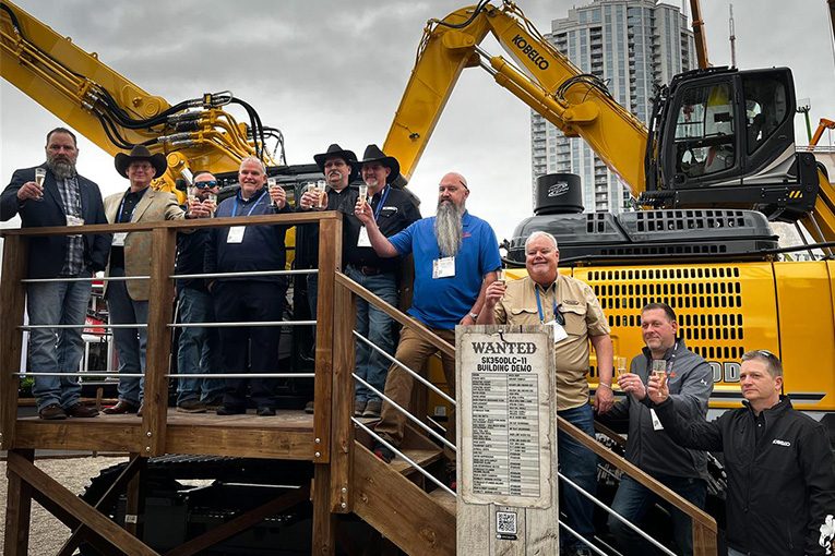 Group of people toasting together on a stage in front of two excavators