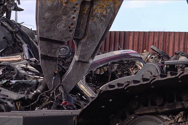 Medium shot of the SK210D-11 Car Demolition Excavator grasping scrap metal.