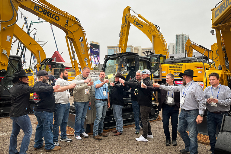 Group of people toasting together in front of an excavator